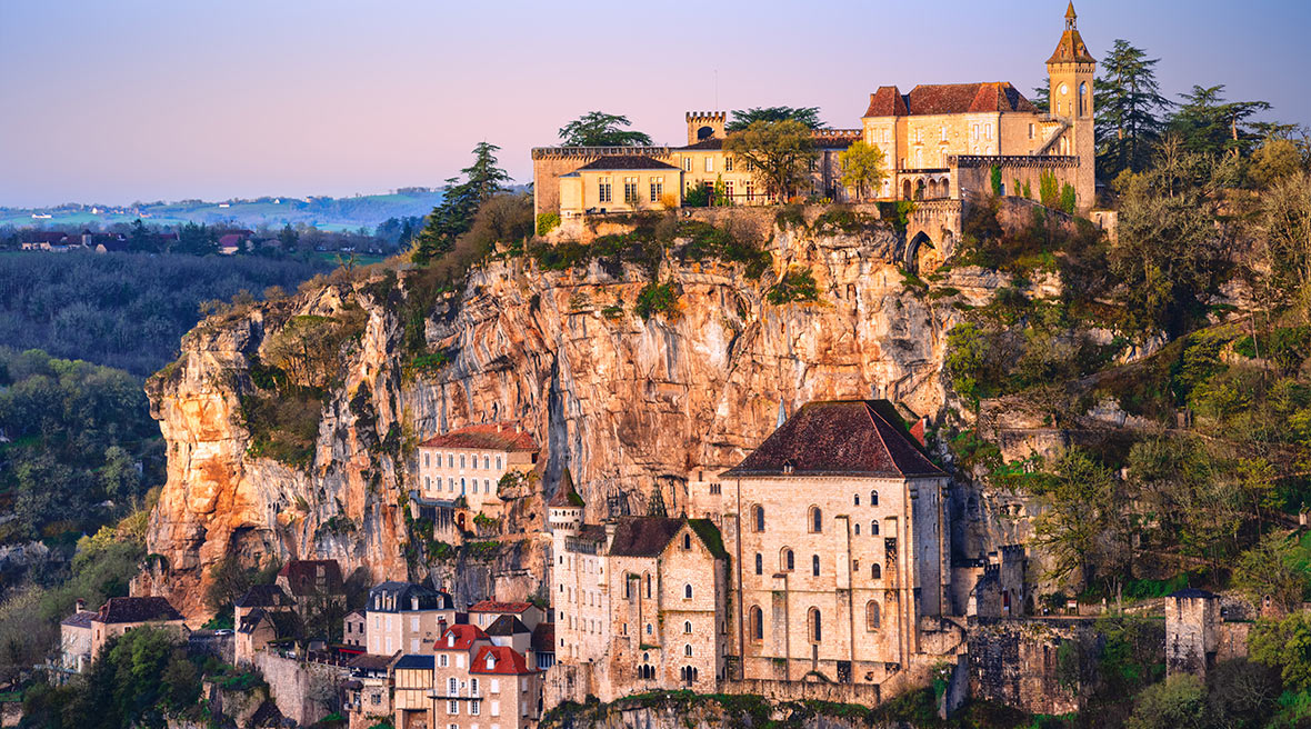 A pretty French village set back into a cliff edge with a lush green valley surrounding it